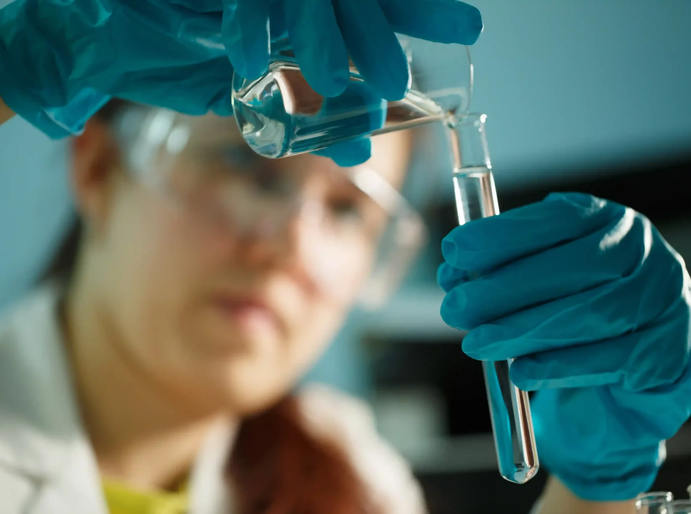 Laboratory technician wearing blue protective gloves transferring liquid between glass laboratory containers.
