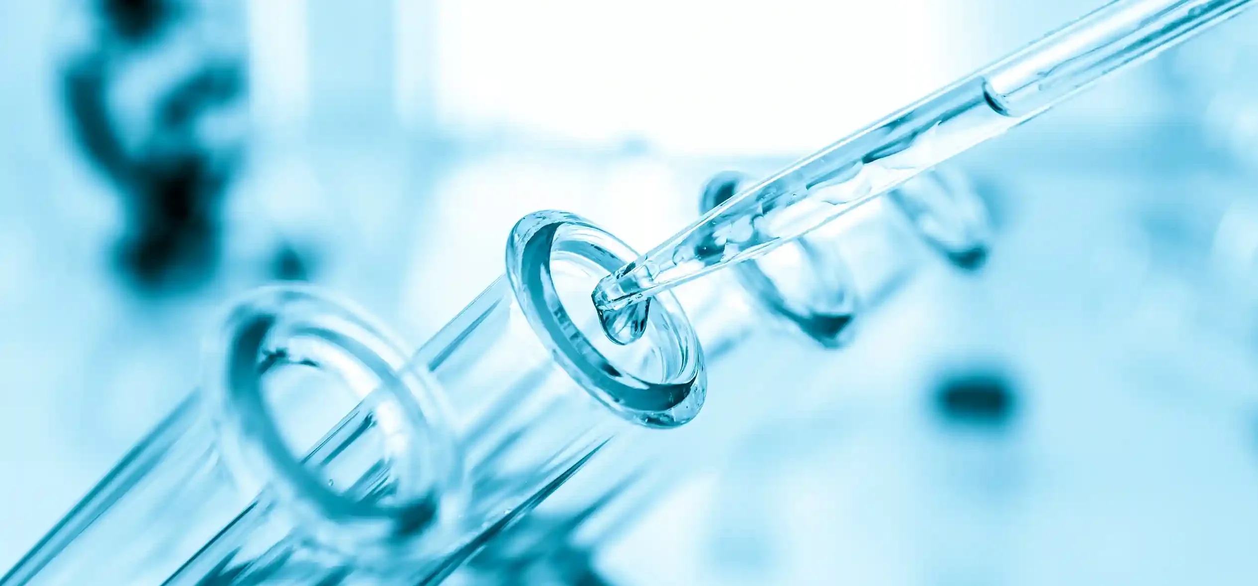 Close-up of transparent laboratory glassware and a glass pipette against a blue-toned laboratory background.