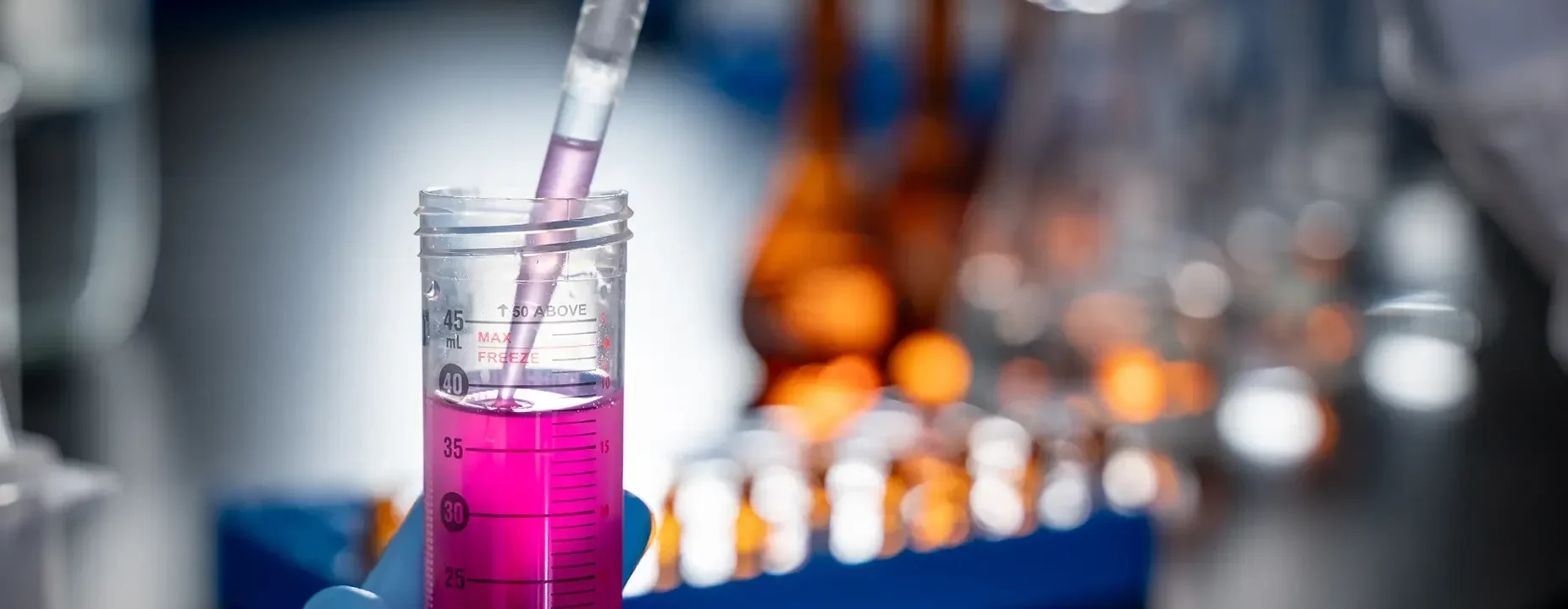 Laboratory technician using a pipette to transfer bright pink liquid into a graduated specimen tube for scientific testing and sample analysis.
